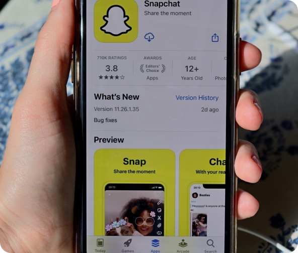 Hand holds a cellphone with the Snapchat app in the App Store on the screen.