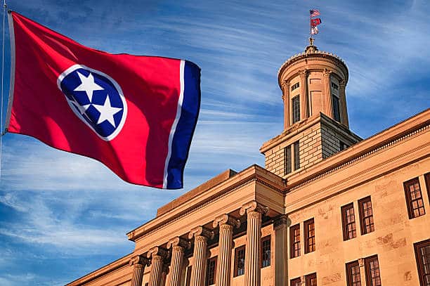 Tennessee state capitol building front exterior in Nashville, with wind blowing the US state flag outside on a partly cloudy day.