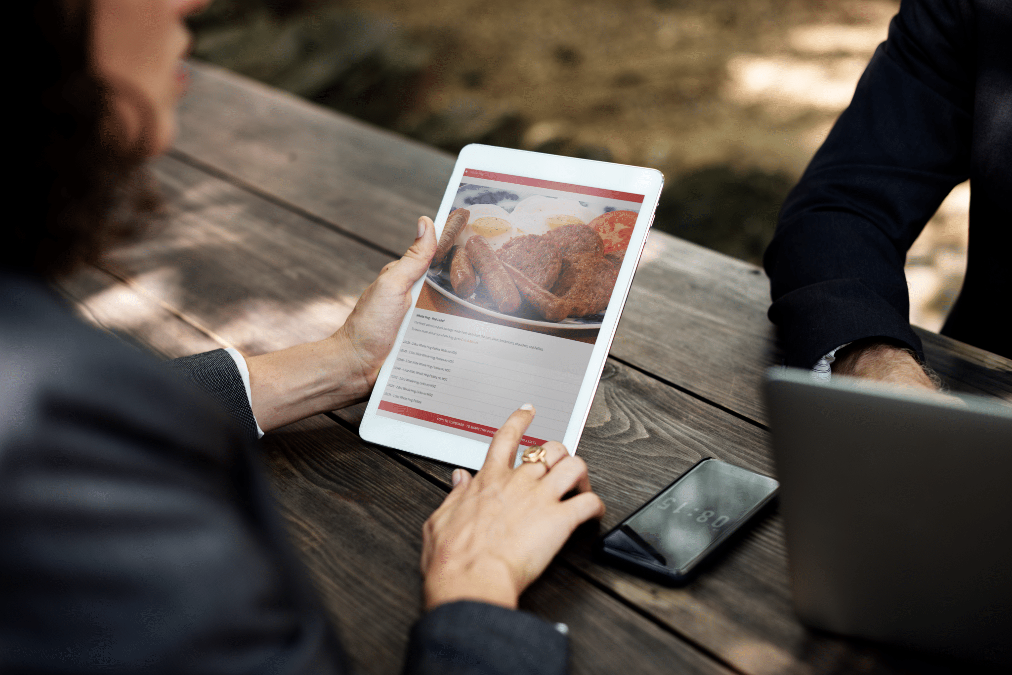 Person sits outside with a tablet in their hands scrolling through the Swaggerty's Sausage website.