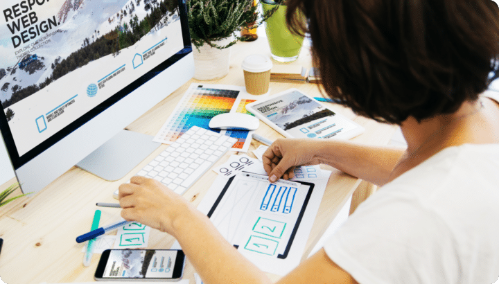 A person sits at a desk with their working on responsive web design, with drawing laid out and markers.