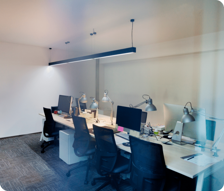 An empty office with monitors turned off, rolling chairs under long tables.