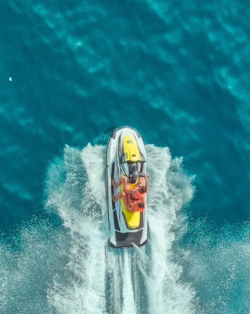 Two people on a yellow, black and white jet ski riding over clear blue water.