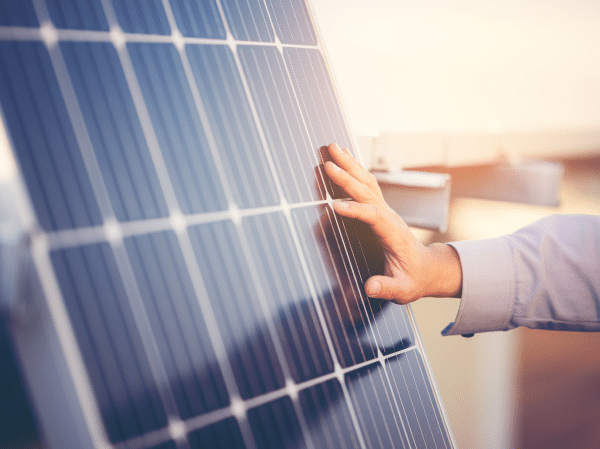 A hand reaches out and touches a solar panel leaning against a roof overhang.
