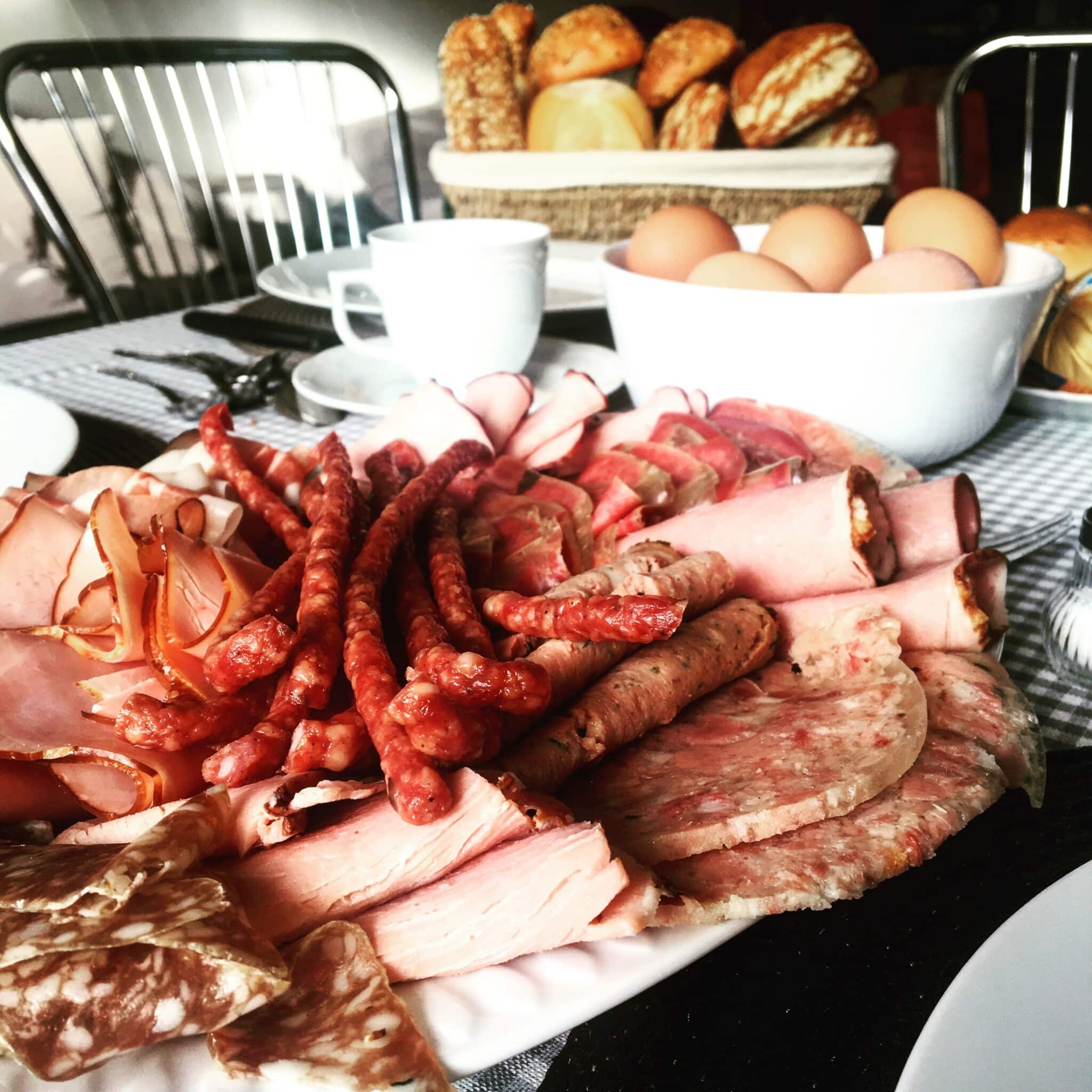 Various meats on a platter with whole eggs and a bread basket on a table.