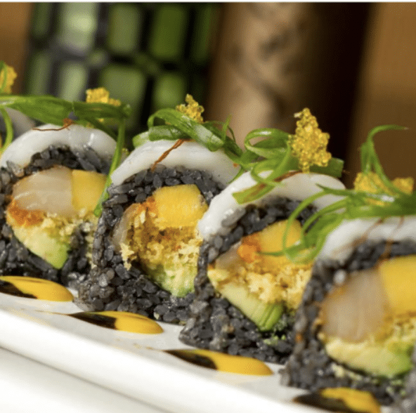 Sushi roll with various colorful ingredients, seaweed on top and a sauce on the plate.