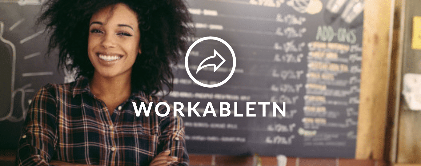 Woman in front of a cafe board smiles ahead with white font reading WORKABLETN and in icon above it.