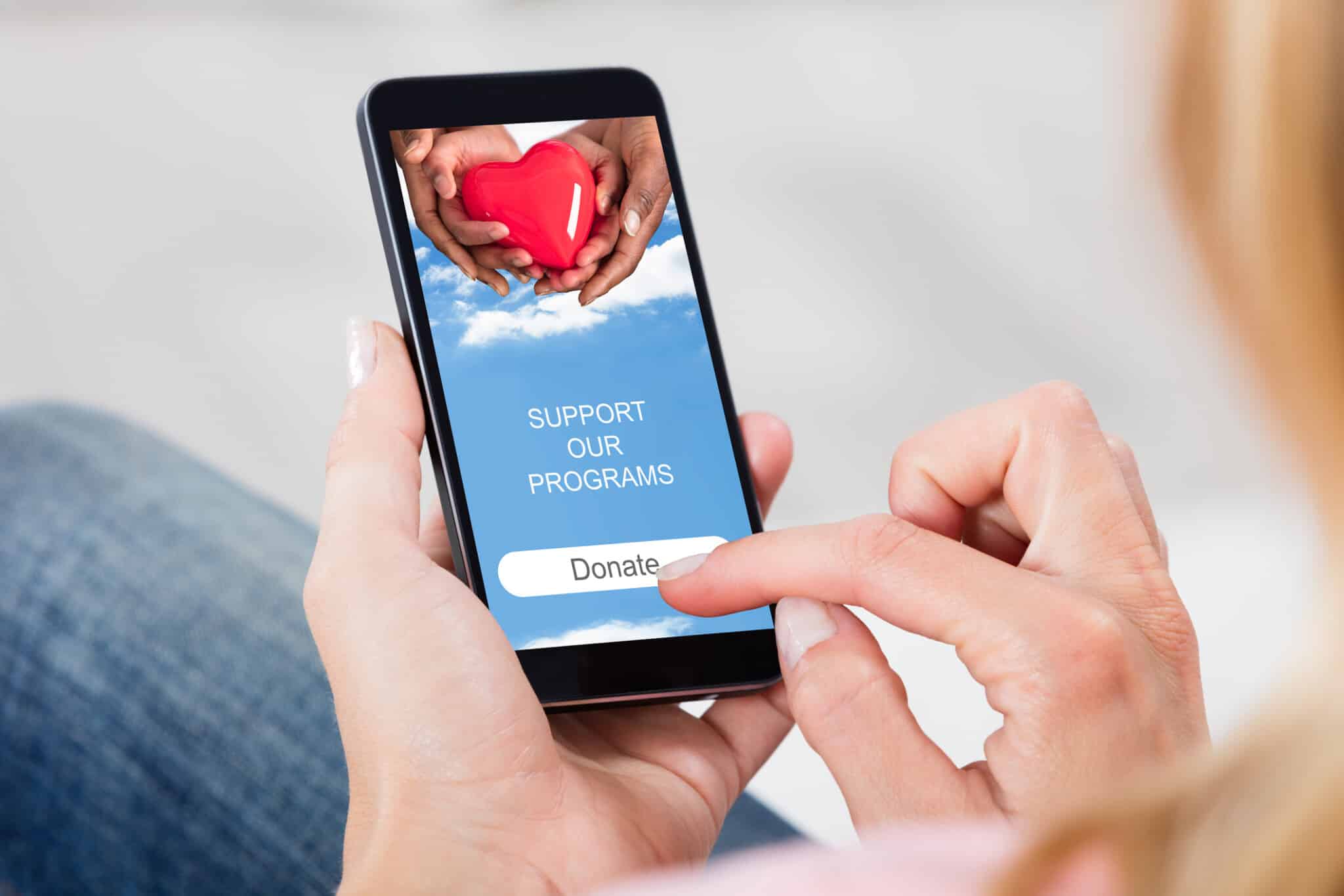 Persona holds mobile phone in hand, scrolling through donation webpage.
