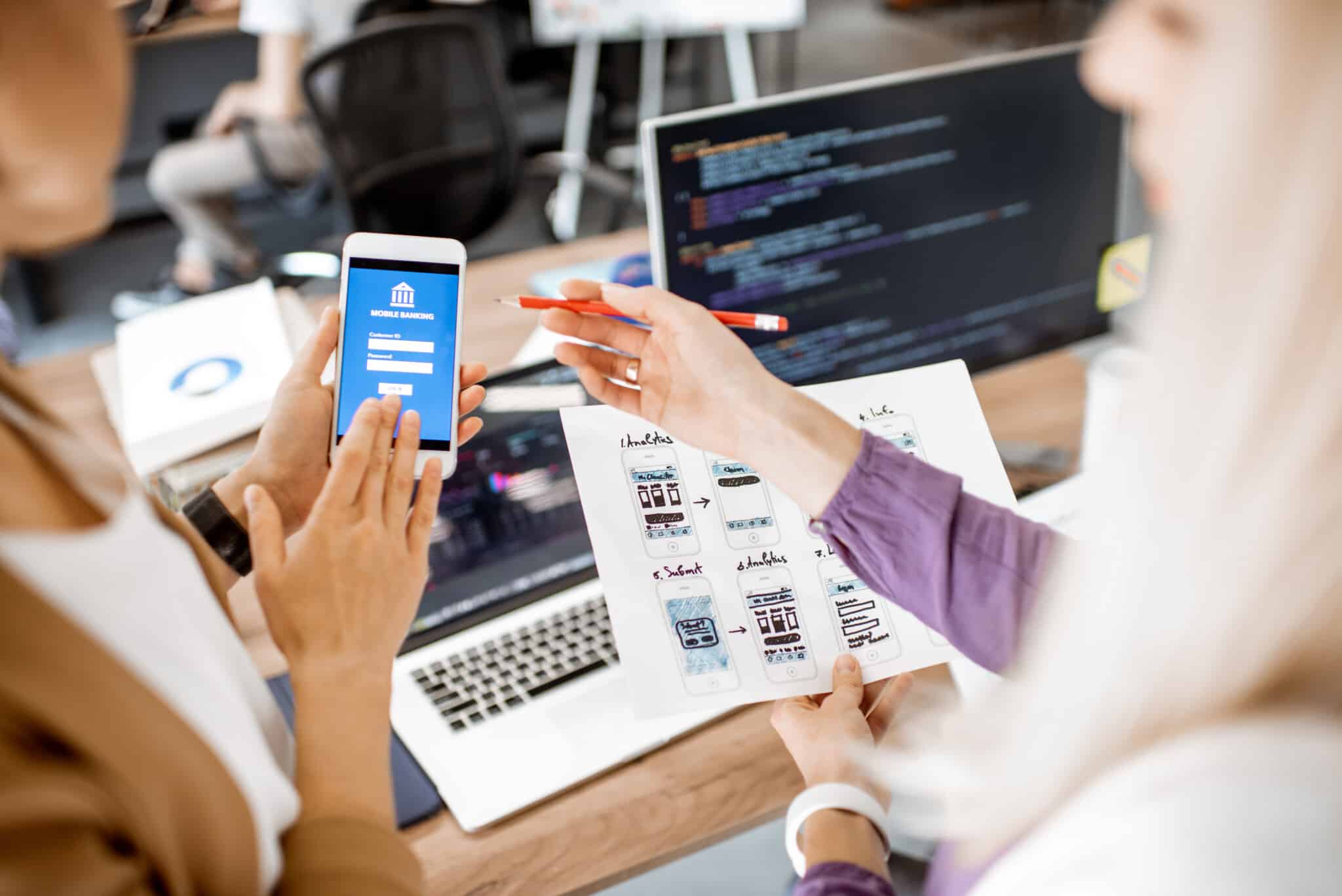 Two people look at a smart phone with designs for an app in one persons hand.