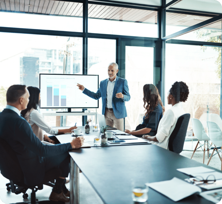 Analysts in a meeting room with one person presenting and others listening showing analysis for customer acquisition cost determination.