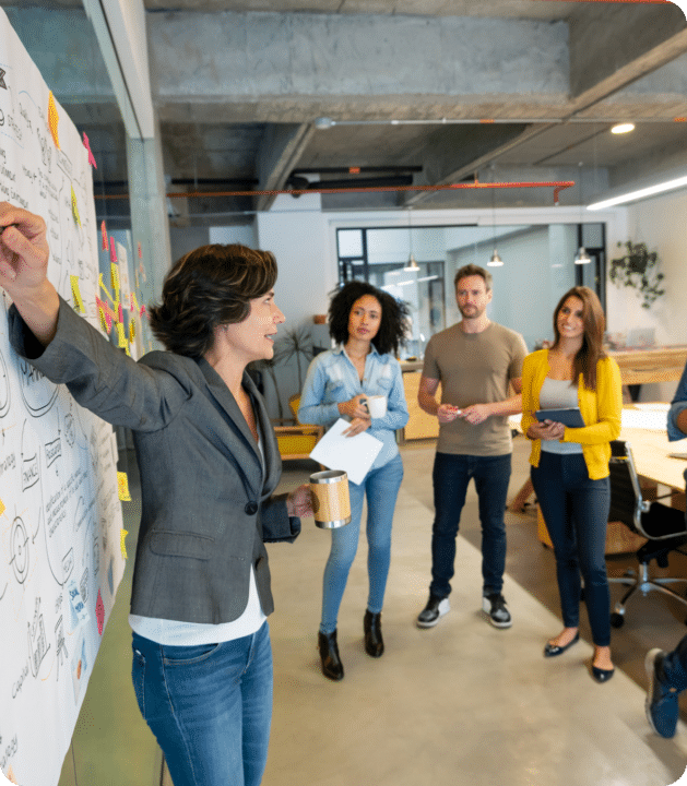 A lady describing ROI-focused Advertising on a whiteboard and other people are standing in a circle around her in an office.